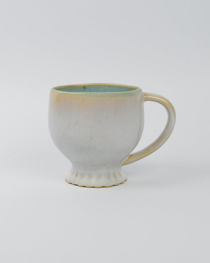 Ceramic mug with handle and scallopd foot and a textured surface on a white background