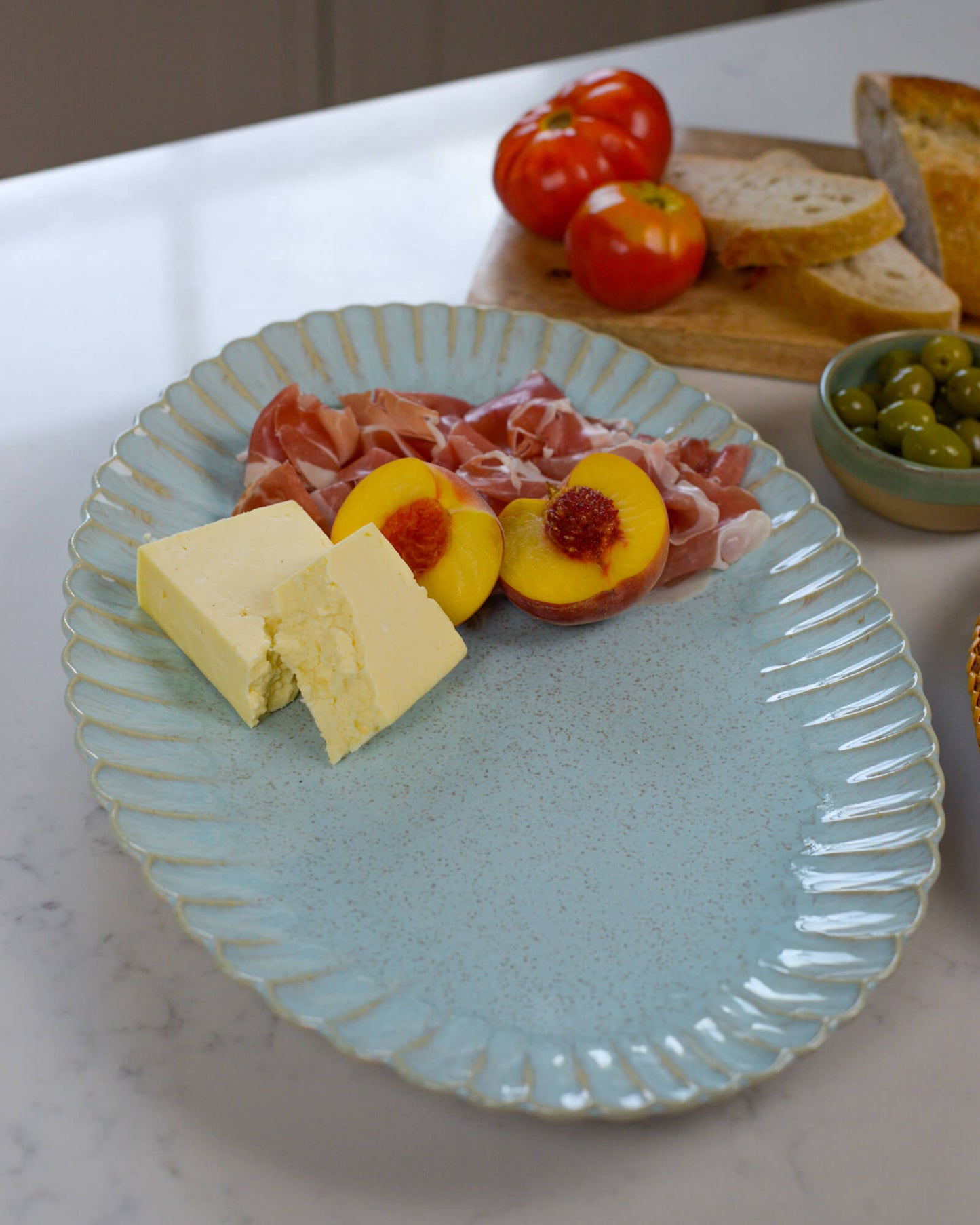 Large oval serving platter with cheese, prosciutto, peaches, and tomatoes on a marble surface.