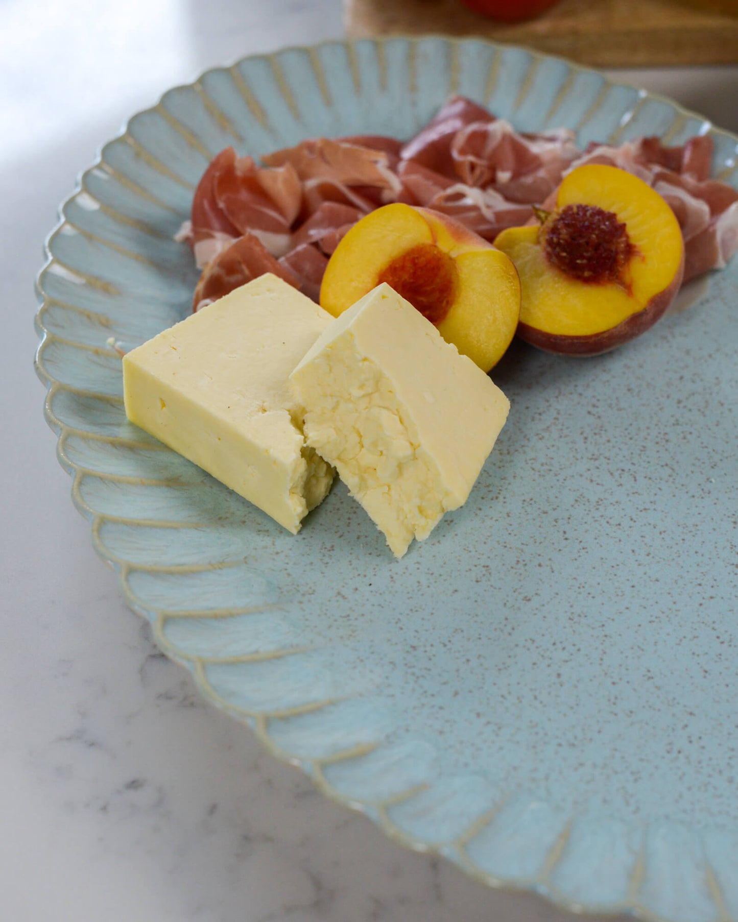 Two blocks of cheese on a decorative serving platter with sliced peaches and prosciutto.