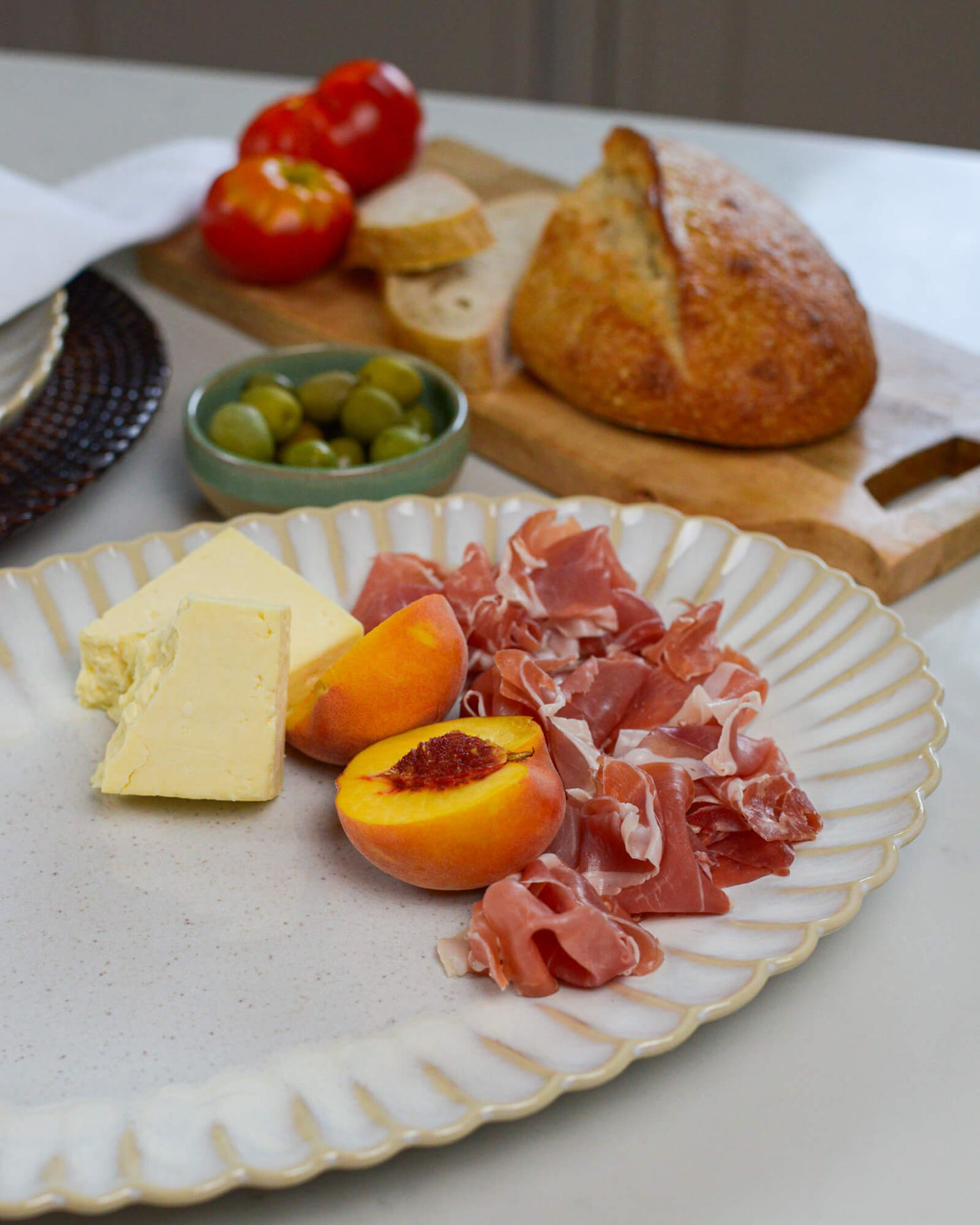Large serving platter with prosciutto, cheese, peaches, and olives on a white marble surface.