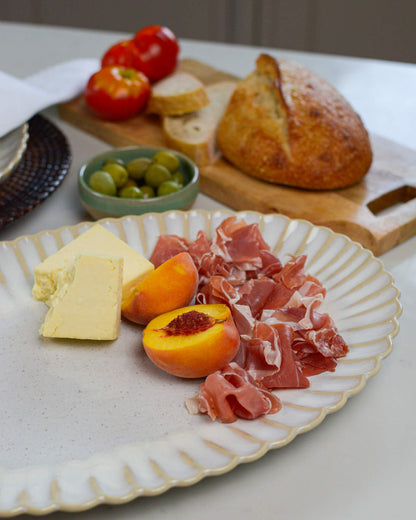 Large serving platter with prosciutto, cheese, peaches, and olives on a white marble surface.