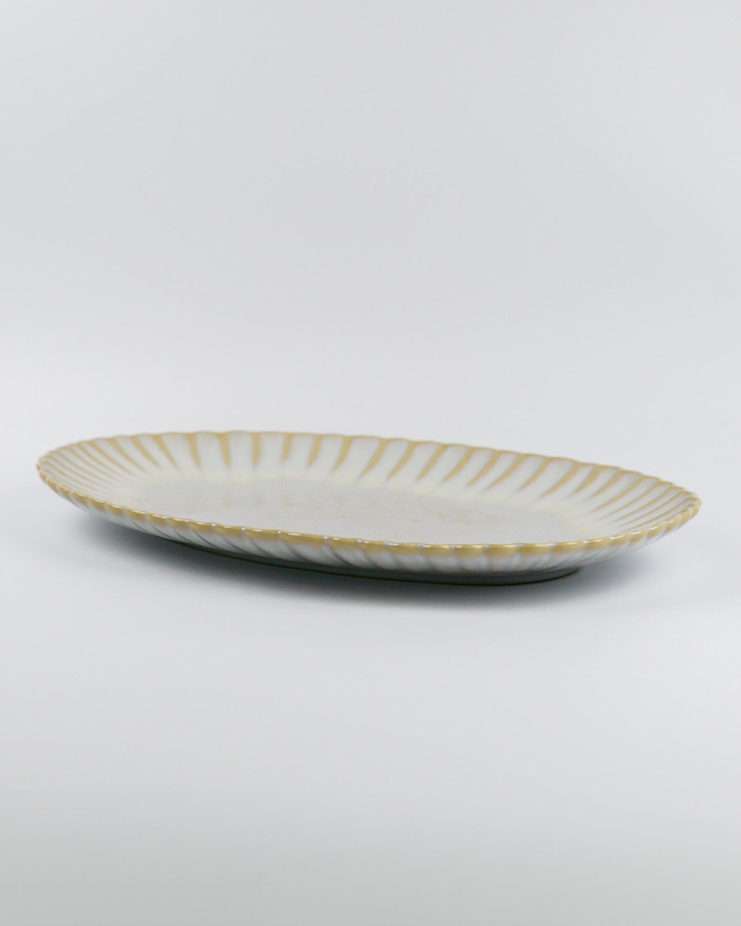 Decorative ceramic oval serving platter with scalloped edge on a white background from the side