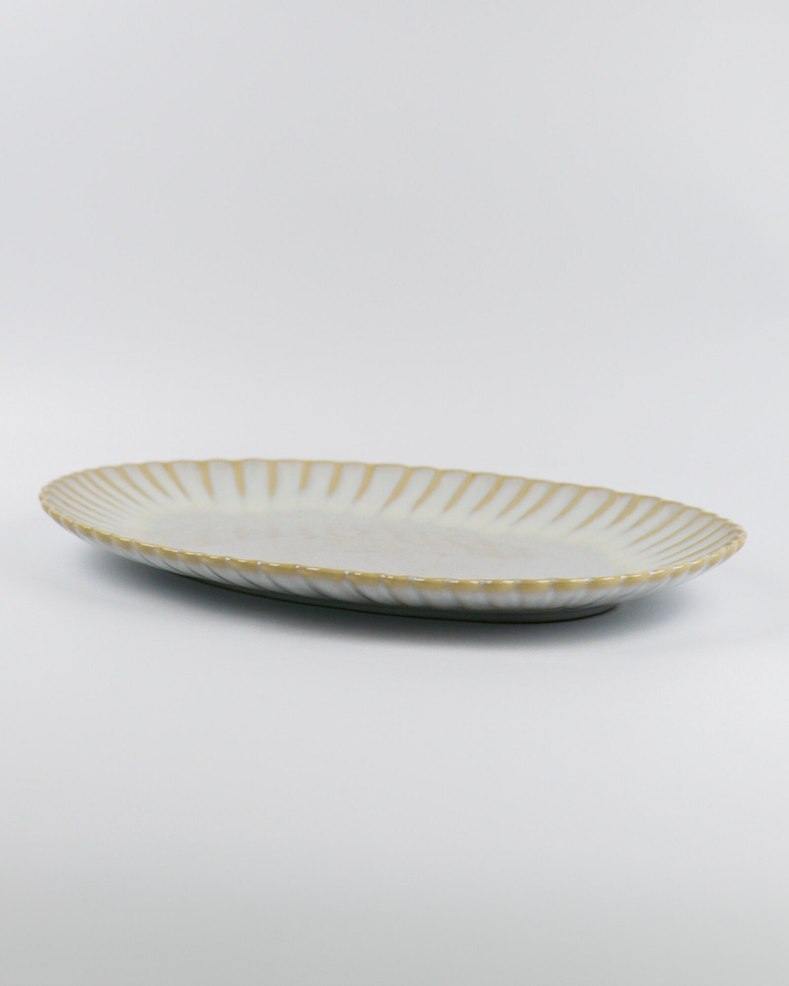 Decorative ceramic oval serving platter with scalloped edge on a white background from the side