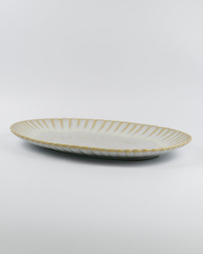 Decorative ceramic oval serving platter with scalloped edge on a white background from the side