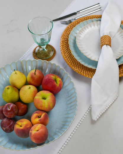 Fruit bowl serving dish with a scalloped edge containing apples, pears, and peaches on a table setting with plates and cutlery.