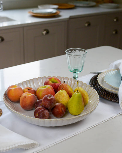 Fruit bowl serving dish with a scalloped edge with apples, pears, and plums on a kitchen counter