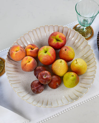 Fruit including apples, peaches, and pears in a decorative serving dish with a glass and coaster in the background.