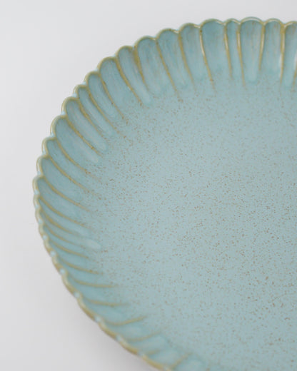 Close-up of a textured blue ceramic serving dish with a scalloped edge on a white background