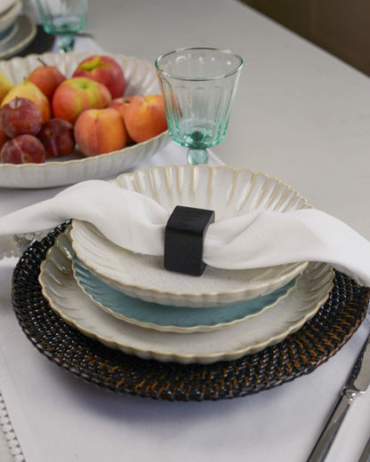 Dining table setting with stoneware pasta bowl, scalloped edged plates, napkin, and fruit bowl in the background.