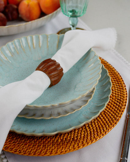 Sky blue ceramic pasta bowl with a shell design on a woven placemat with a white napkin.