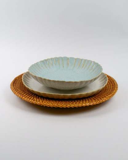 Set of ceramic scalloped edge pasta bowl and matching plates on a woven rattan charger plate with a white background