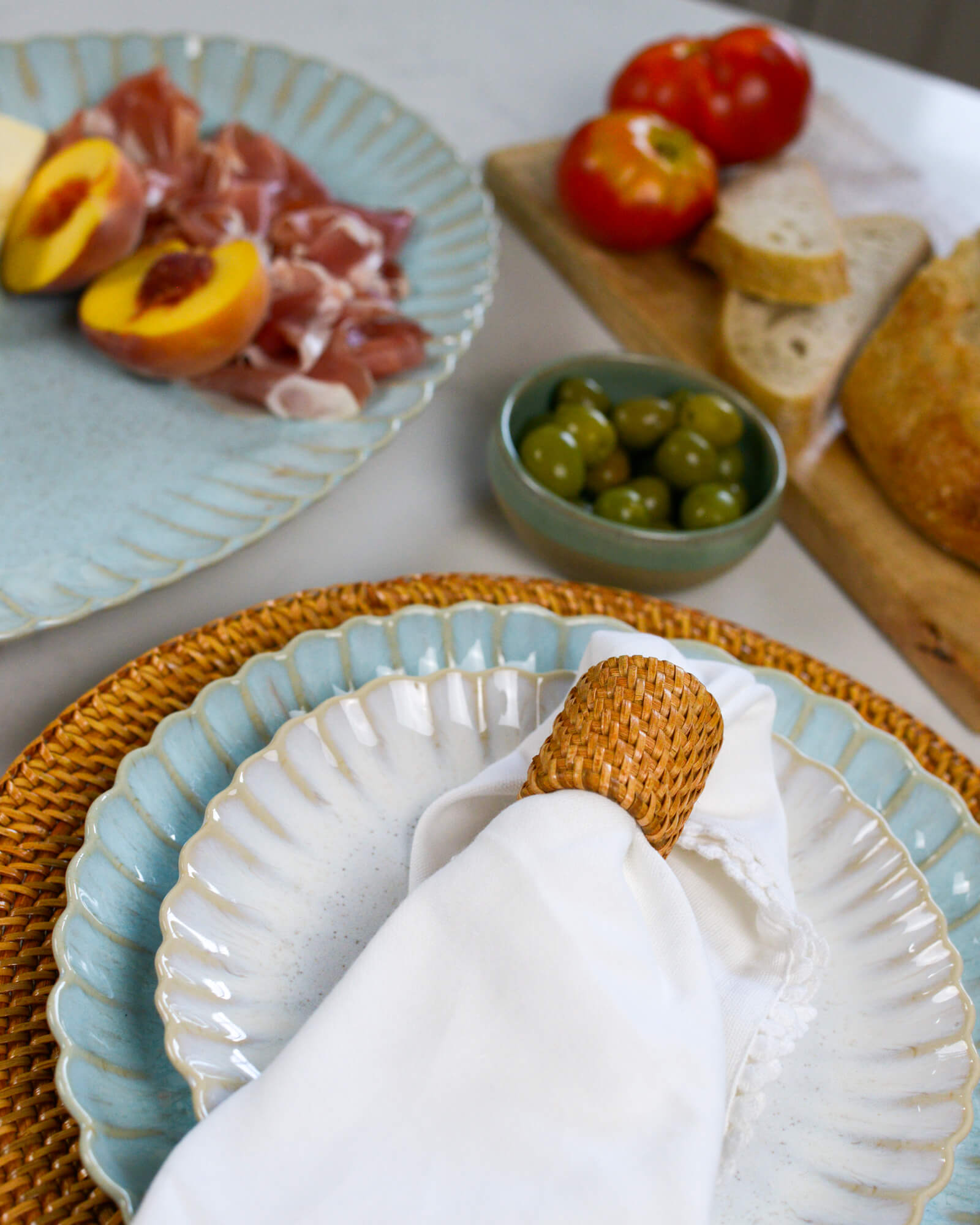 Table setting with ceramic, stoneware plates, bread, olives, and peaches on a white table.