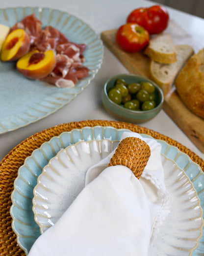 Table setting with ceramic, stoneware plates, bread, olives, and peaches on a white table.
