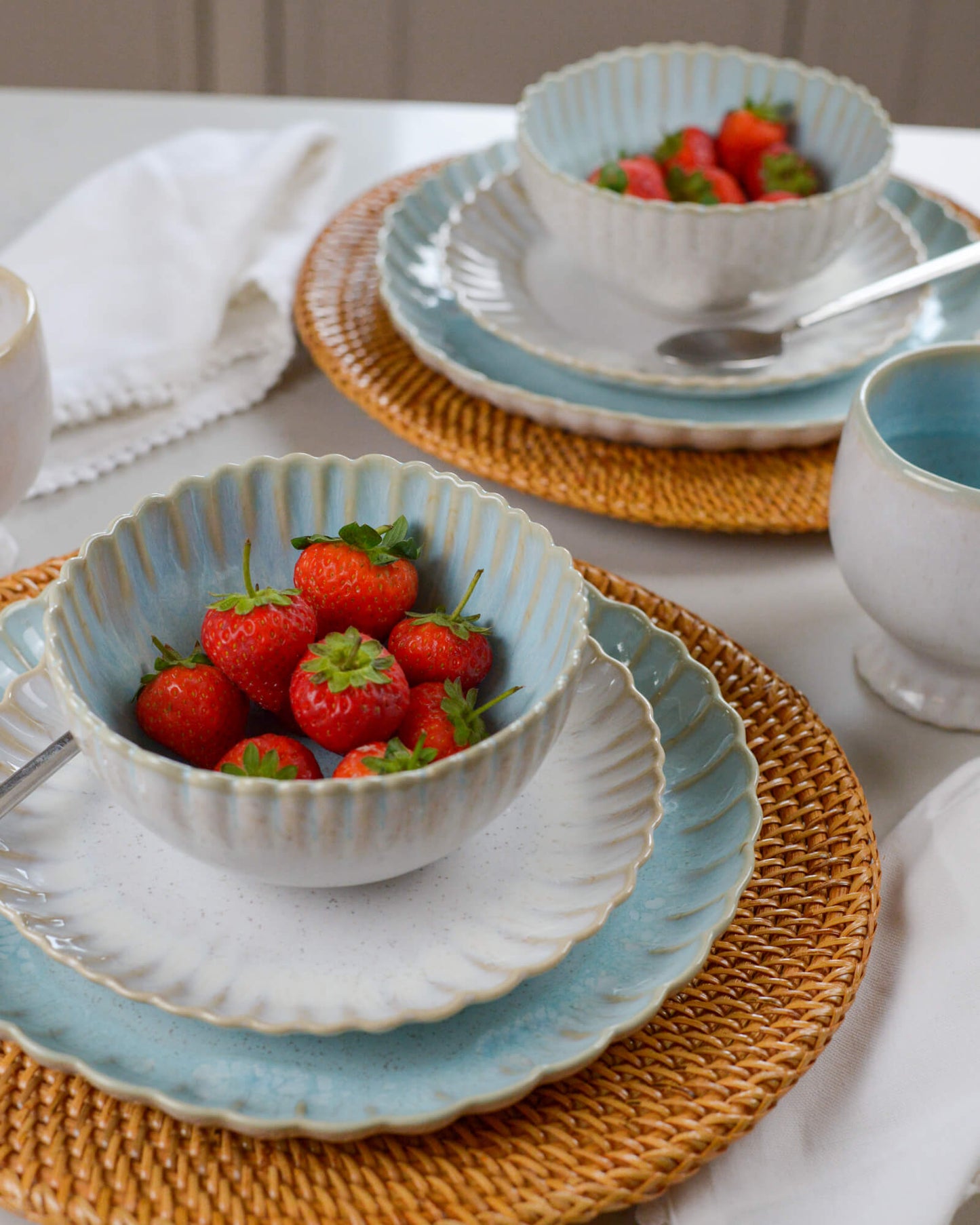 Ceramic stoneware bowls and plates with a scalloped edge containing strawberries on a table setting.