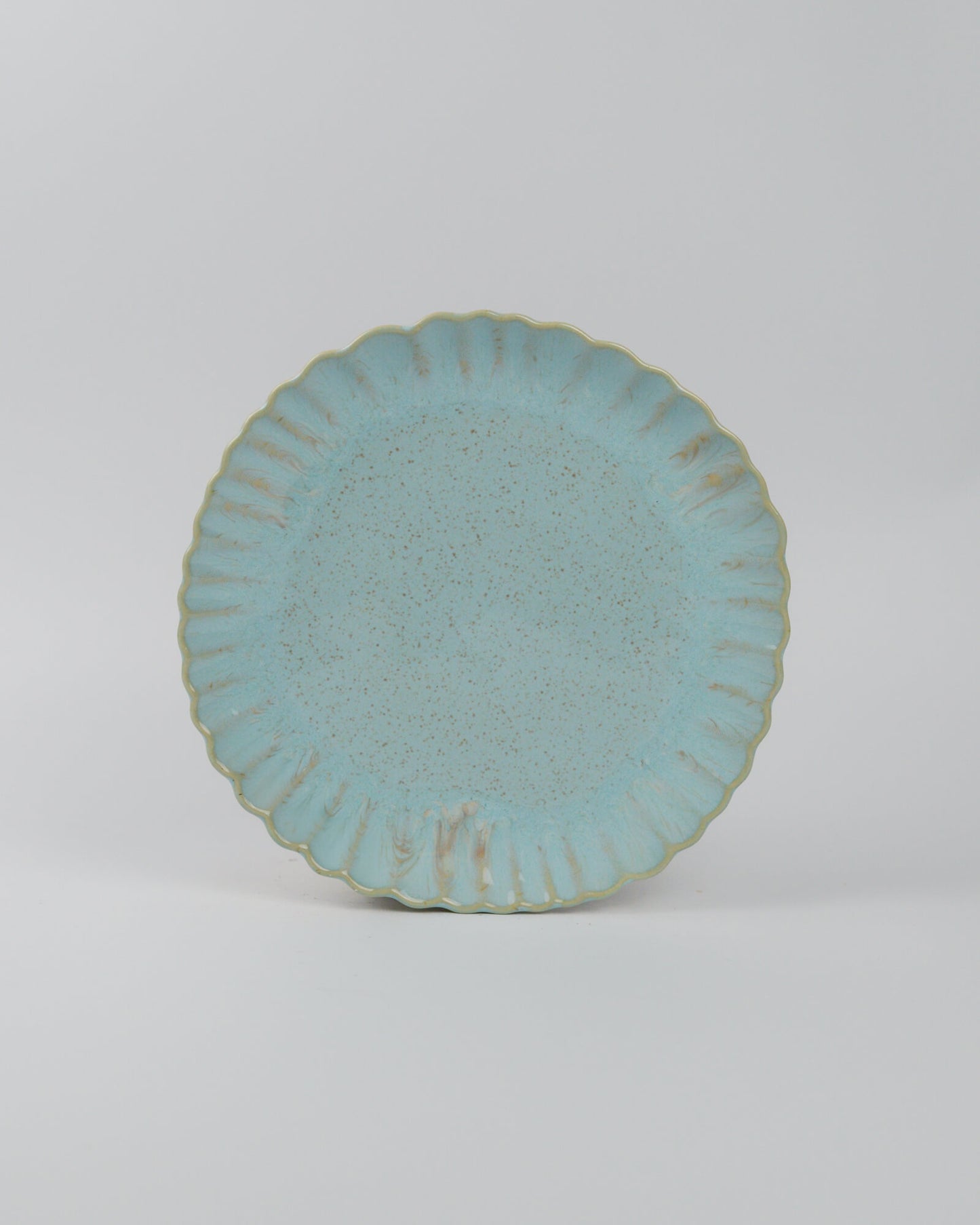 Light blue ceramic plate with textured glaze and scalloped edge on a white background