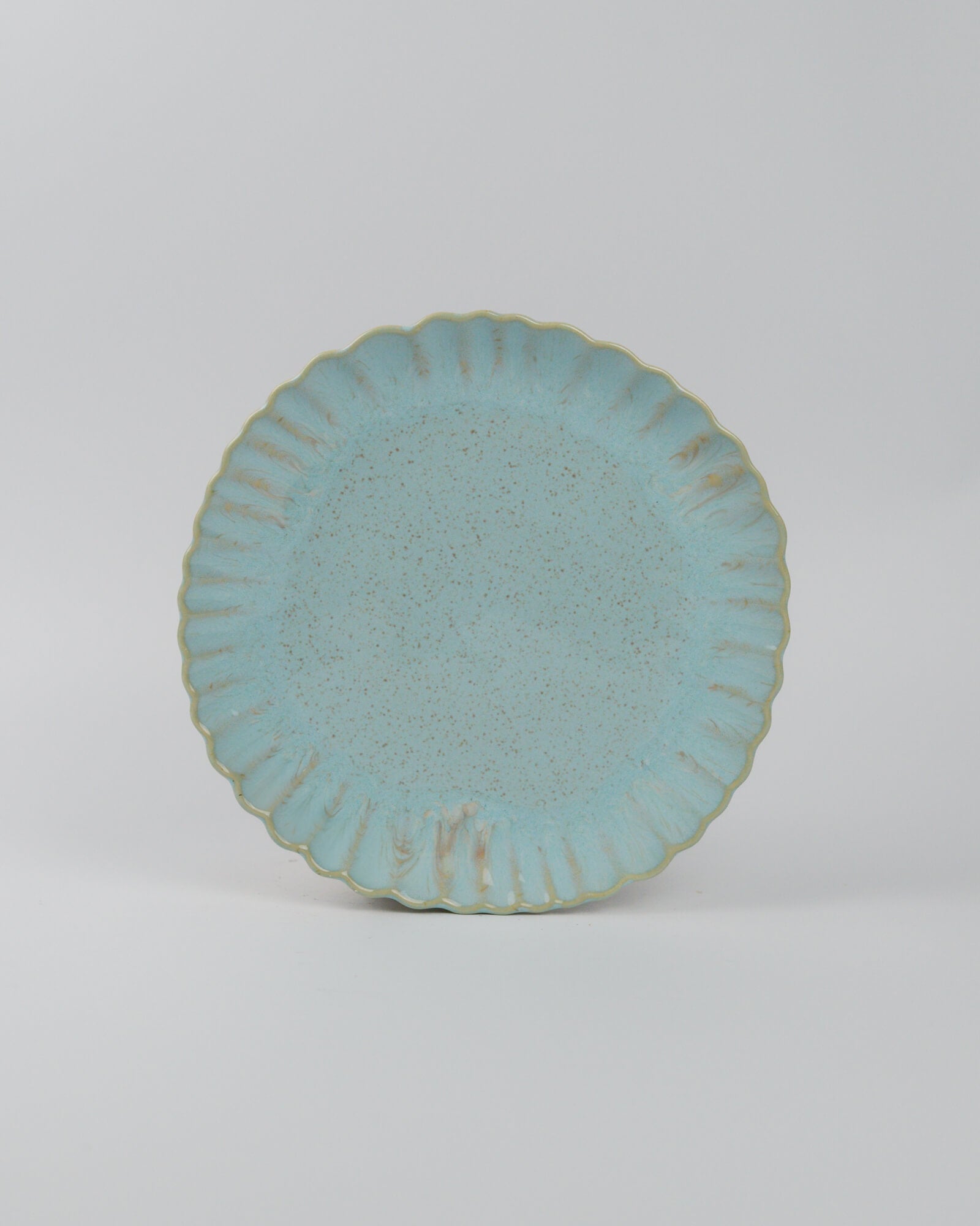 Light blue ceramic plate with textured glaze and scalloped edge on a white background