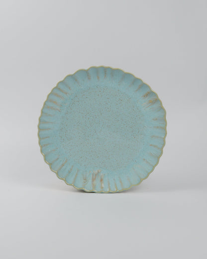Light blue ceramic plate with textured glaze and scalloped edge on a white background