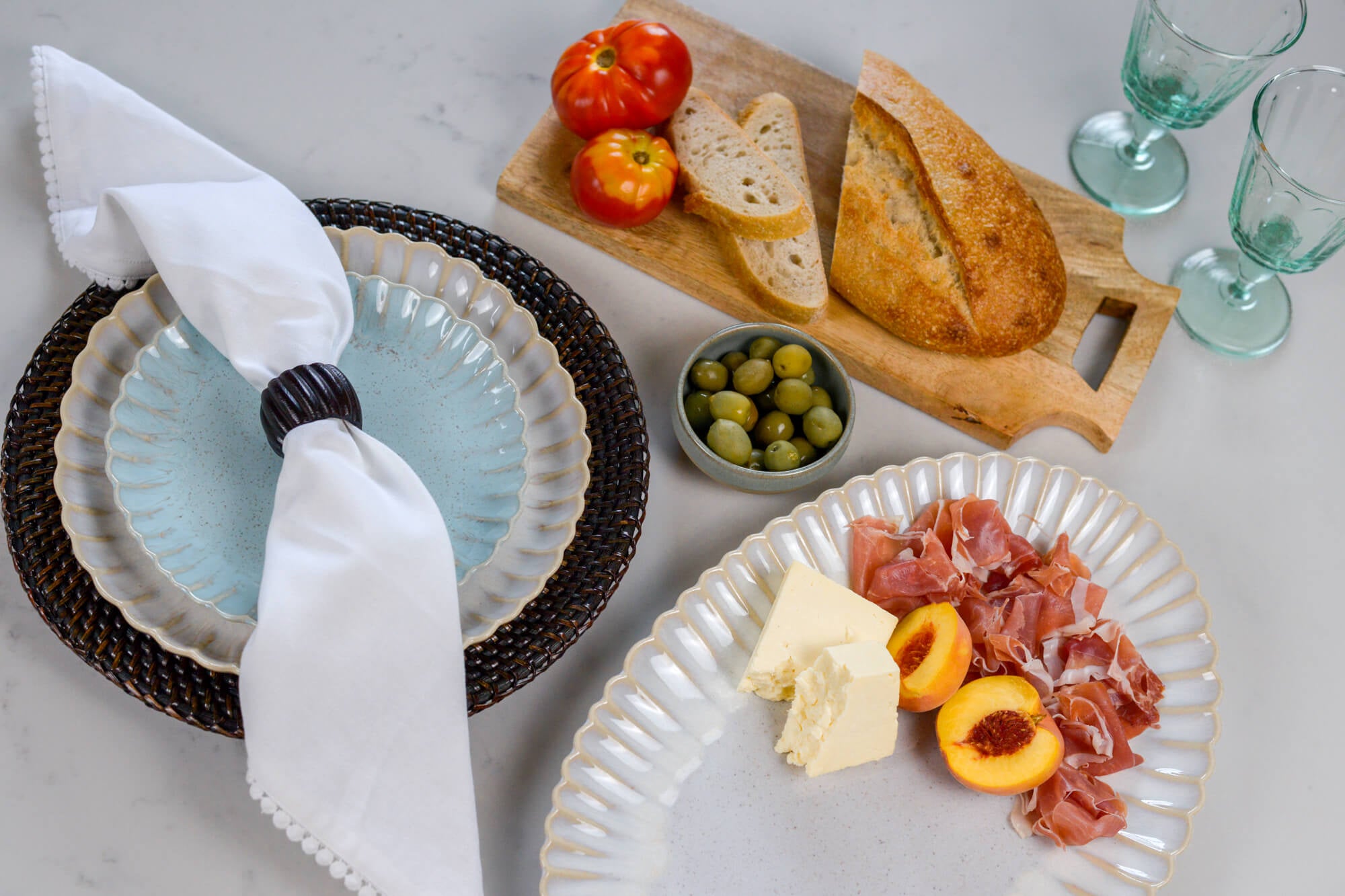 Mediterranean food on scalloped stoneware plates with bread, olives, and peaches on a marble surface