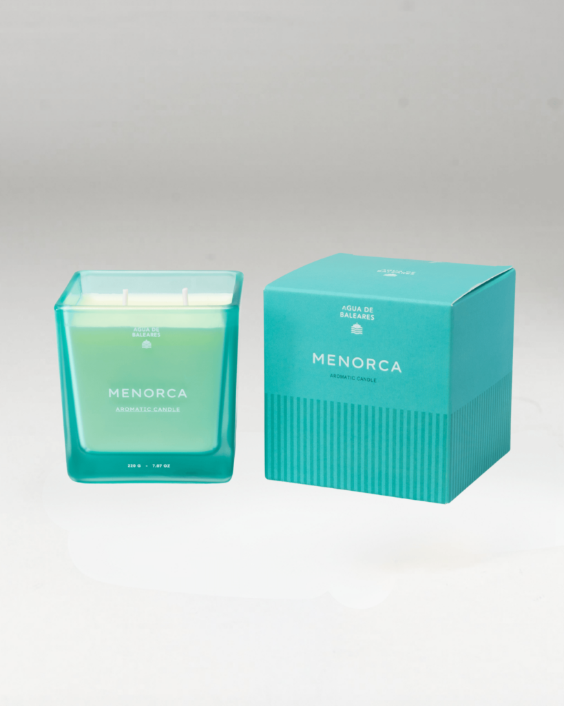 A teal glass jar candle labeled MENORCA stands beside its matching teal box on a clean white studio background.