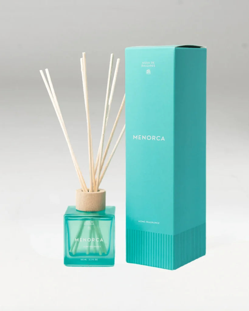 A Menorca reed diffuser with a turquoise glass bottle, natural wood reeds, and a tall matching turquoise box on a white background.