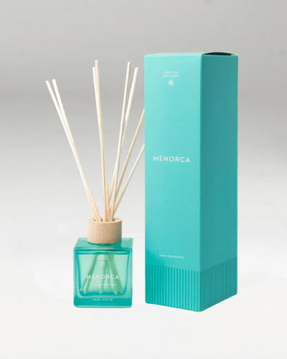 A Menorca reed diffuser with a turquoise glass bottle, natural wood reeds, and a tall matching turquoise box on a white background.