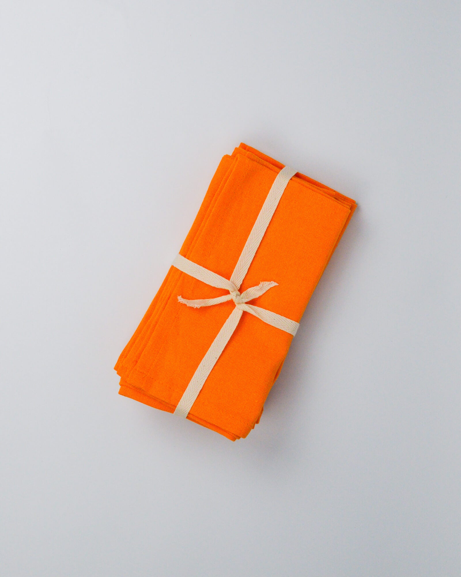 Orange folded orange cotton, linen blend napkins with a white ribbon on a white background