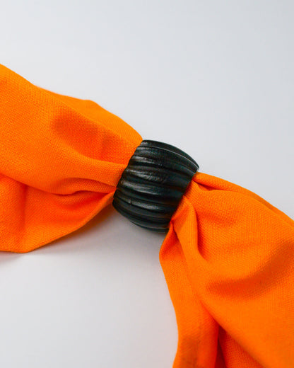Orange cotton napkin held with a dark wooden ribbed wooden napkin ring on a white background