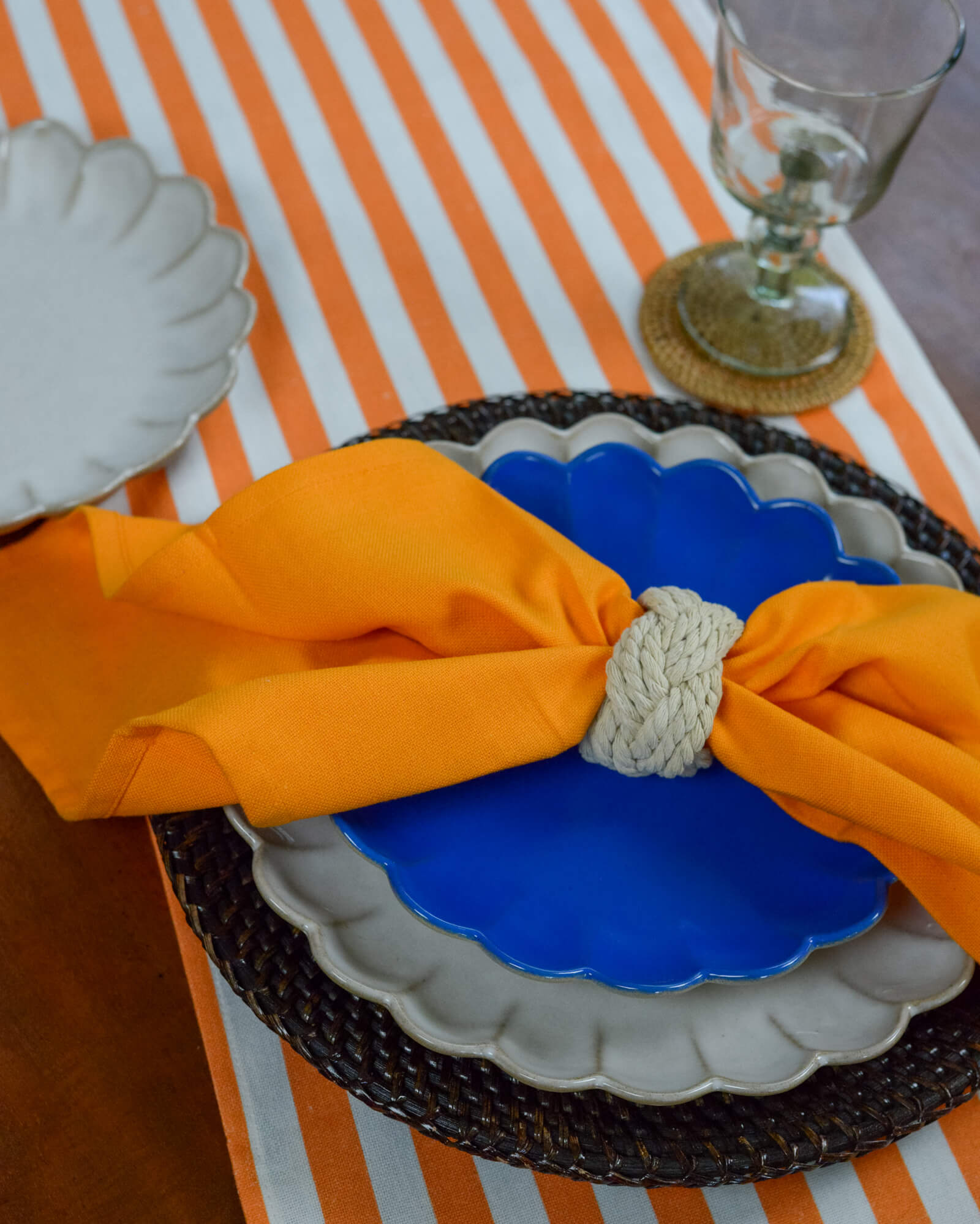 Decorative table setting with blue plate, orange cotton napkin, and orange and white striped table runner.