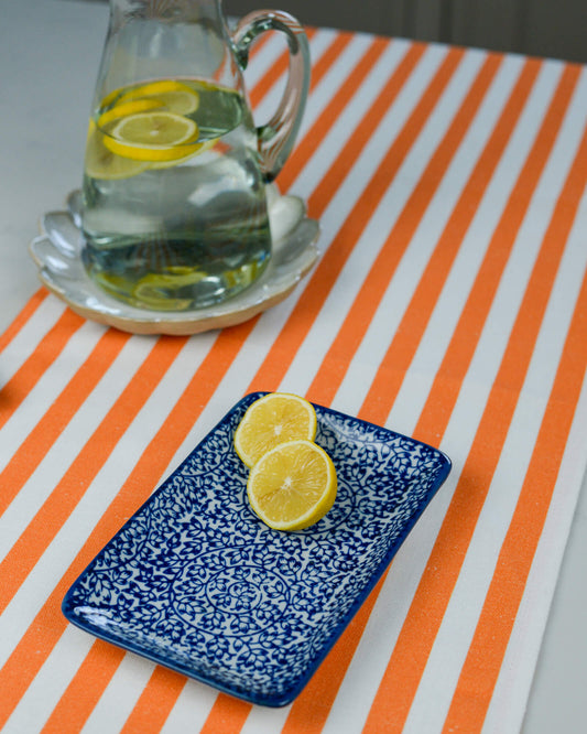 Clear pitcher with lemon slices on a striped orange table runner