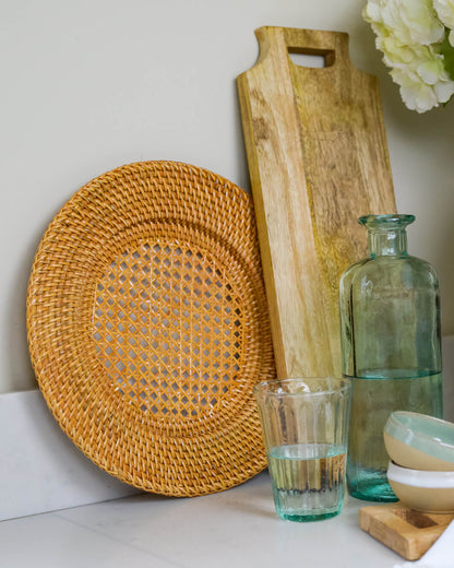 Decorative items including a woven rattan plate, wooden cutting board, glass bottle, and ceramic vase on a surface.