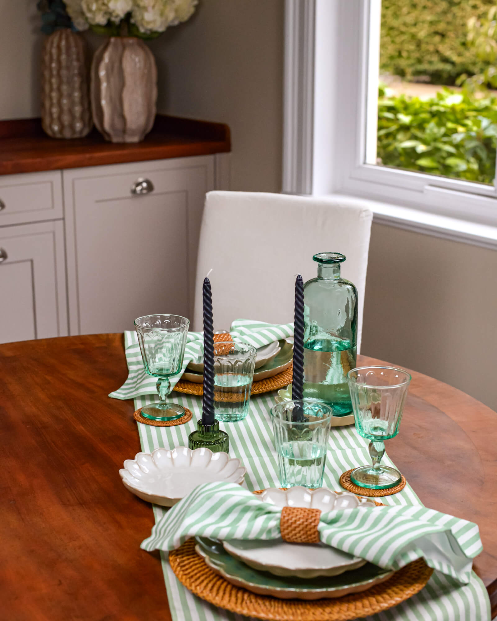 Dining table set with green glasses, candles, and striped napkins in a home setting.