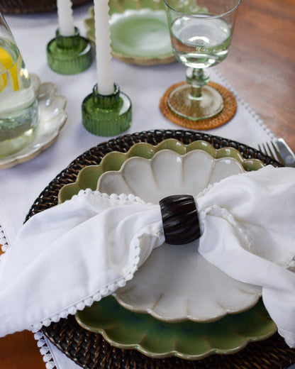 Decorative table setting with a white napkin, dark wooden napkin ring, and green ceramic plate.
