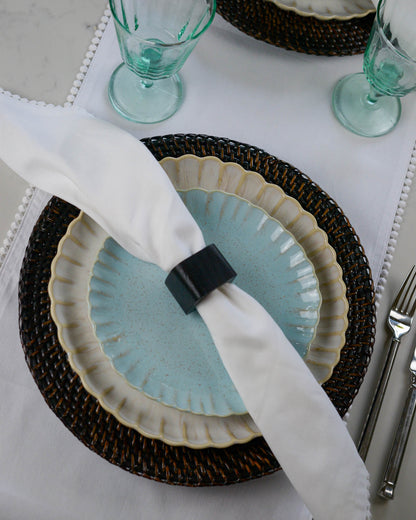 Table setting with a dark wooden napkin ring holding a white napkin over a blue plate.