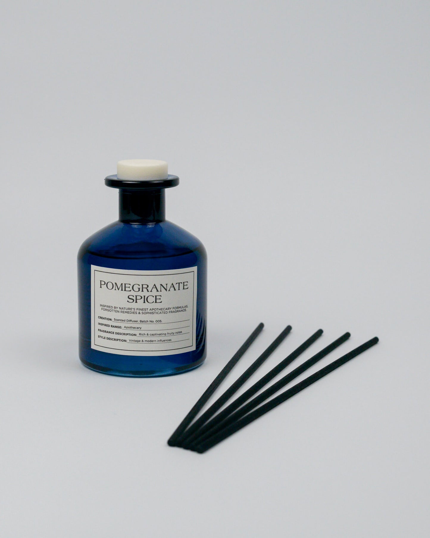 Blue bottle labeled 'Pomegranate Spice' with black sticks on a white background
