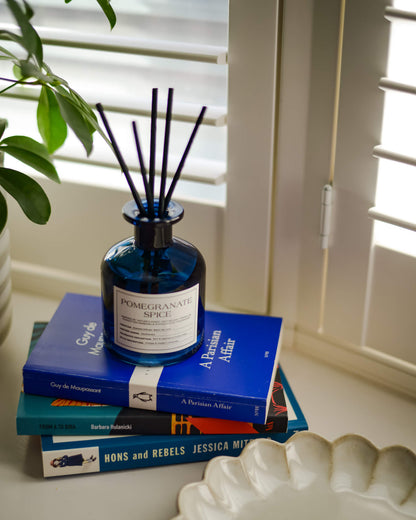 Blue pomegranate spice diffuser bottle on books with a plant in the background