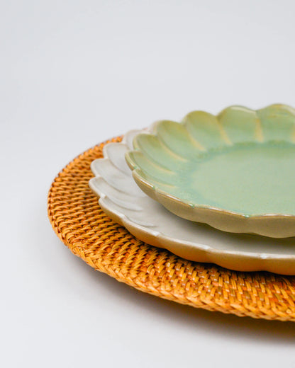 Stack of ceramic plates on a woven rattan charger plate with a white background