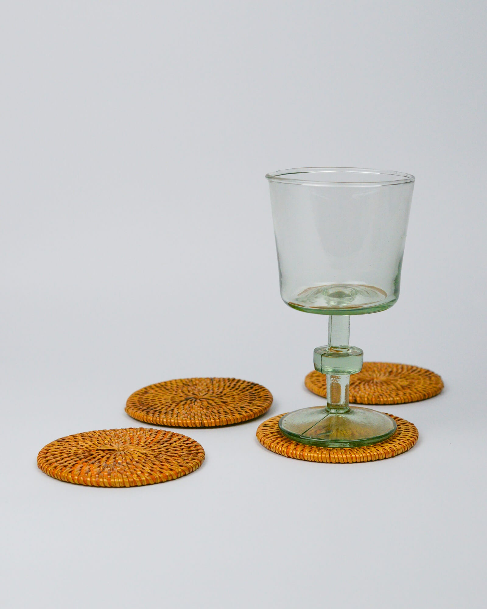 Clear glass with green base on rattan woven coasters against a white background