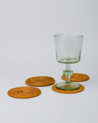 Clear glass with green base on rattan woven coasters against a white background