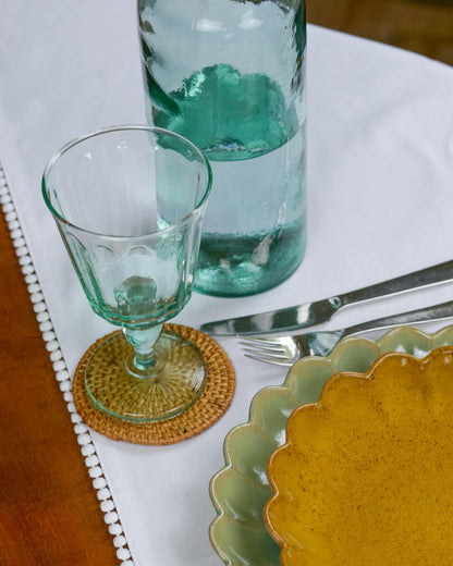 Table setting with a glass, coaster, and ceramic plate on a white tablecloth.