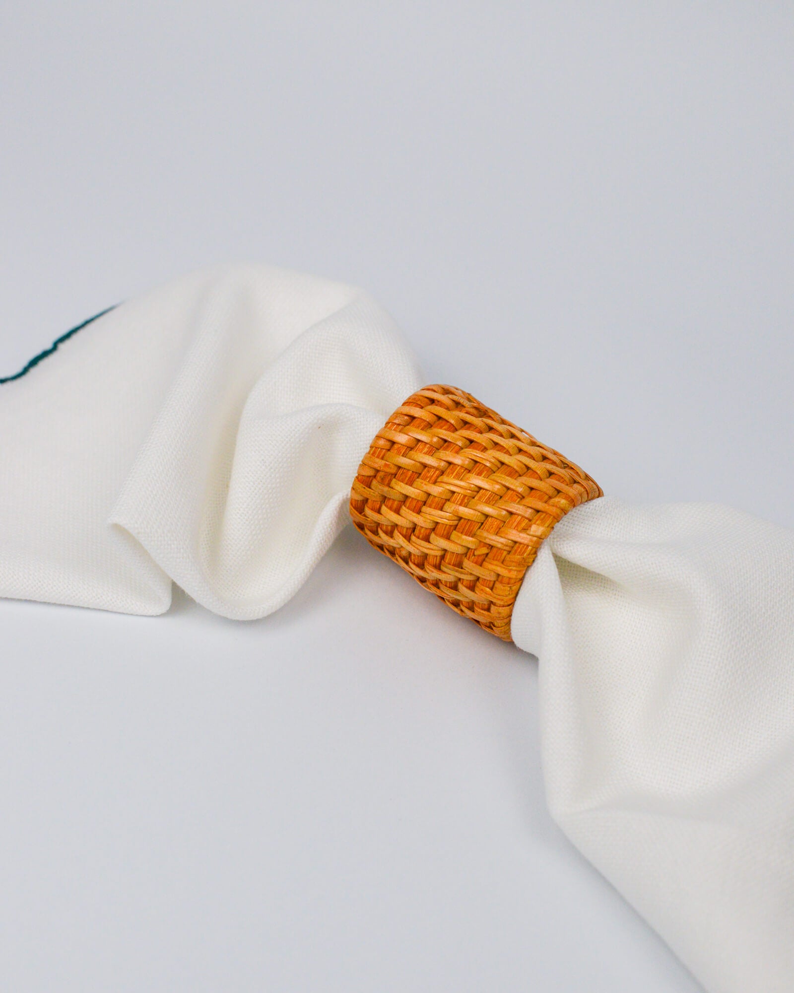Rattan woven napkin ring on a white background with white linen napkin