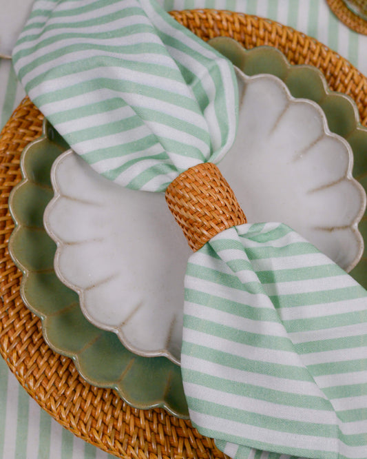 Green and white striped napkin on a scalloped edge plate with rattan napkin ring
