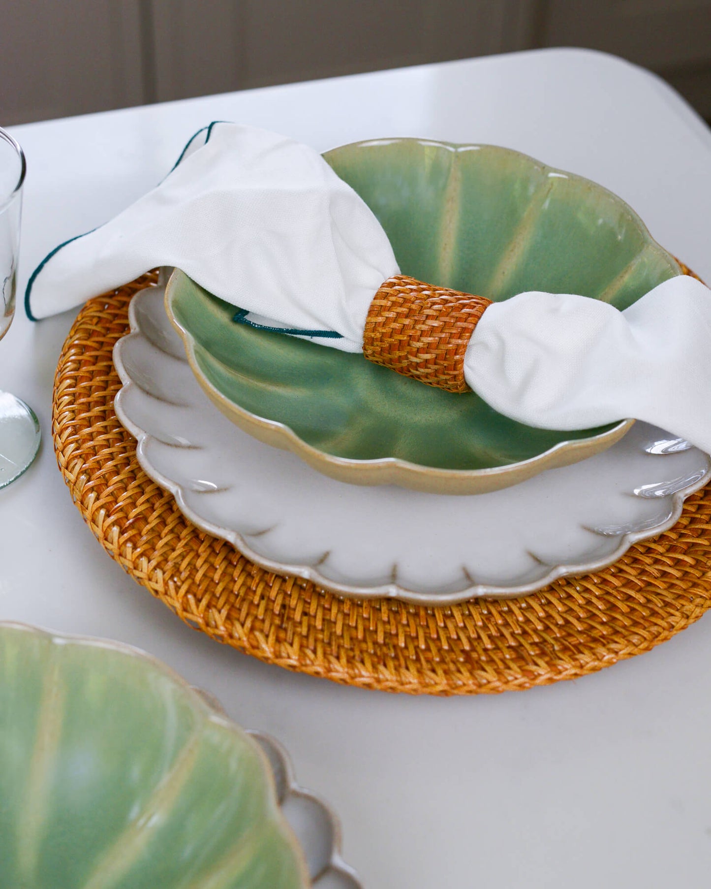 Green ceramic plate with a white napkin being held with a rattan napkin ring