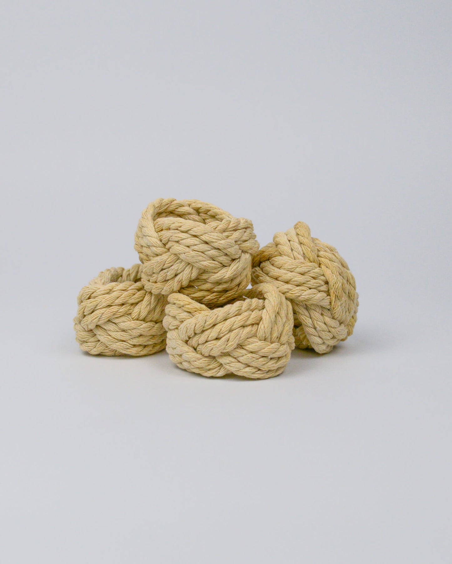 Four natural coloured rope napkin rings stacked on a white background