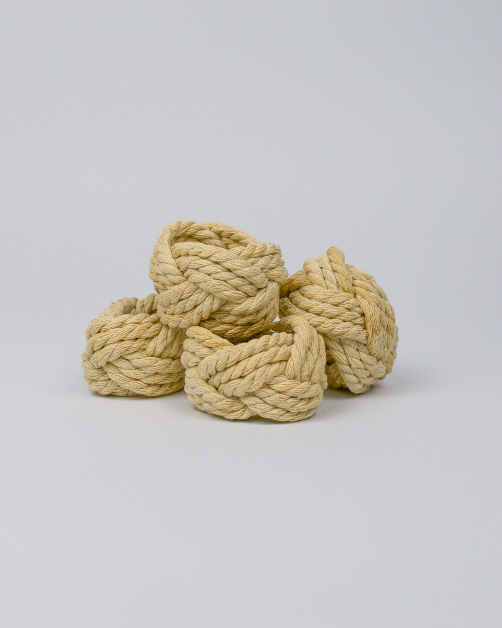 Four natural coloured rope napkin rings stacked on a white background