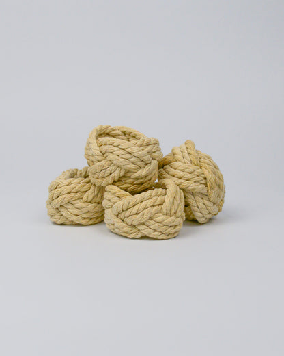 Four natural coloured rope napkin rings stacked on a white background