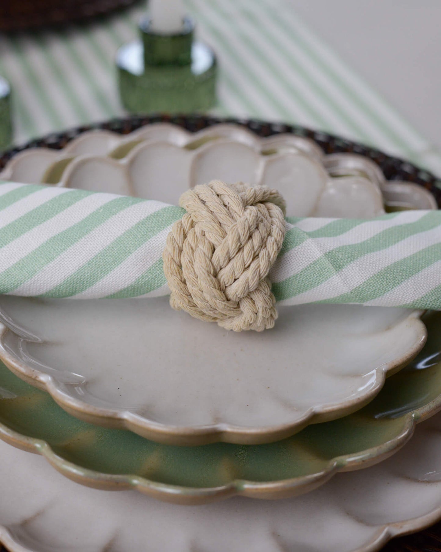 Rope Napkin Ring holding a green striped cotton napkin on a white scalloped side plate