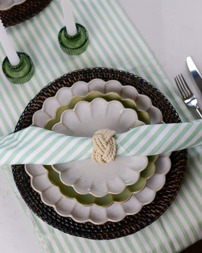 Table setting with green and white striped table runner, scalloped edge plates, and cutlery on a white table.