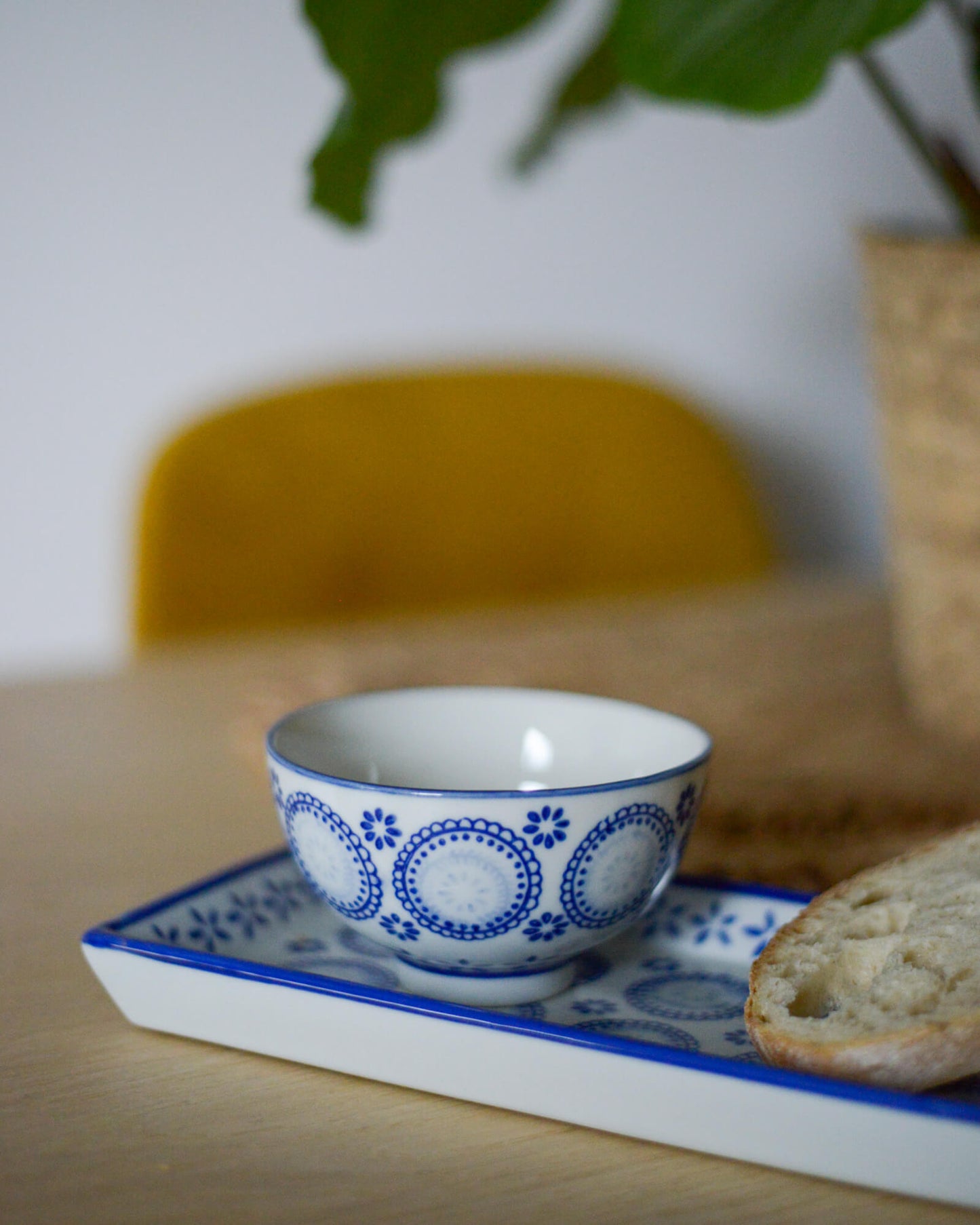 Blue and white ceramic bowl on a matching ceramic rectangular tray with bread on a wooden table.