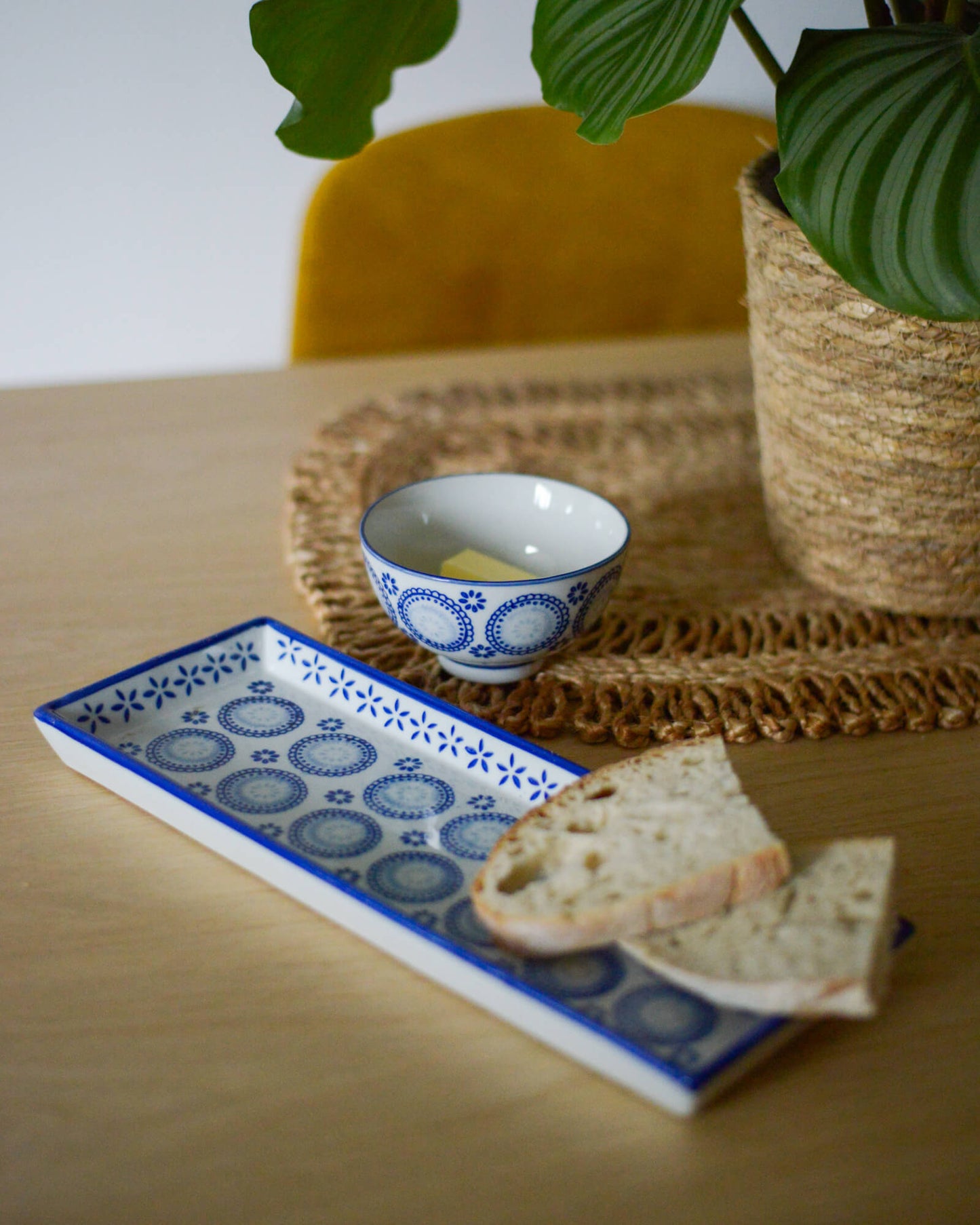 Small ceramic bowl with bread on a decorative plate on a wooden table with a plant in the background