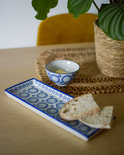 Small ceramic bowl with bread on a decorative plate on a wooden table with a plant in the background